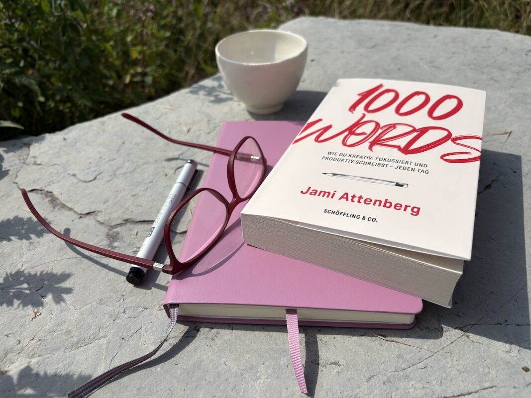 Buch "1000 words" als Stilleben mit Journal, Stift und Brille